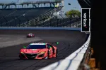 Red Acura race car speeding on an empty racetrack with Verizon advertisement on the barrier.