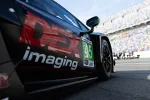 Black race car with DEX Imaging branding and number 45 parked at a colorful grandstand racetrack.