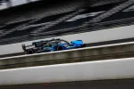 Blue and black race car speeding on a professional race track with blurred background and grandstands.