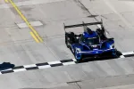Blue Acura race car crossing the checkered finish line on a concrete race track in daylight