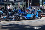 Acura Konica Minolta race car number 10 in pit stop with crew performing maintenance during race event.