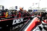 Close-up of a sleek DEX Imaging Acura race car at a crowded racing event with drivers and fans in the background.