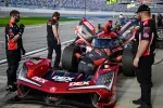 Pit crew performs maintenance on red Acura race car during motorsport event with officials overseeing.
