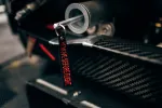 Close-up of a carbon fiber part with a key featuring a red 'REMOVE BEFORE FLIGHT' tag hanging from a metal ring.
