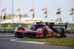 Red and black Acura prototype race car number 40 speeding on track with blurred background and flags.