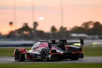 Red and black race car with DEX imaging logo speeding on a racetrack during sunset with blurred background.