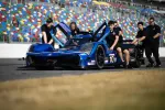 Blue Acura NSX electric race car pushed by team members on racetrack with colorful grandstand background