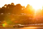 Race car speeding on track during vibrant sunset with blurred crowd and trees in background