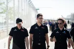 Three men in black Acura DEX Racing shirts walking and talking along a fenced pathway at a race event.