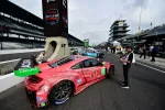 Red Acura race car number 93 in pit lane at a motorsport event with crew and officials nearby under cloudy sky