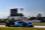 Blue and black race car number 10 speeding on a racetrack under clear sky during daytime.