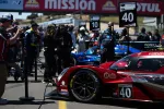 Red and blue race cars lined up on the grid with pit crew and officials preparing at a racing event under Mission and Motul banners.