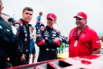 Race car drivers and team member in black and red uniforms standing by a red race car at the racetrack.