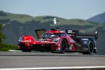 Red and black Acura prototype race car number 40 speeding on a track with mountains in background