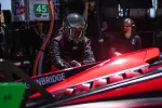 Race car mechanic in black helmet working on a red race car in a pit crew during daytime event