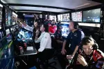 Race team engineers and strategists monitoring multiple screens and data during a motorsport event in a dimly lit control room.