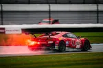Red Acura NSX GT3 race car number 93 speeding on wet track with flames shooting from exhaust at a motorsport event.