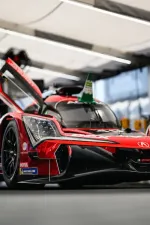 Red Acura prototype race car with open door in a well-lit garage or pit area.