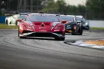 Red race car leading other sports cars on a curving track during a race event.