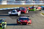 Red Acura race car leads multiple high-speed cars on a curved race track during daytime.