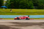 Red race car number 93 speeding on racetrack with green trees and blue barriers in background.