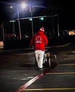 Worker in red jacket painting red line on asphalt parking lot at night under streetlights.