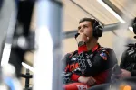 Focused race car engineer wearing headset and team uniform monitoring a race from the pit wall.