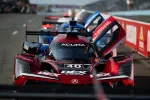 Red Acura race car number 40 with open door in pit lane at a motorsport event.