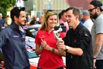 Three people engage with a smartphone on a gimbal at a motorsport event with race cars in the background.