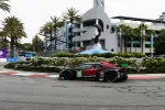 Black and red DEX Imaging race car number 45 speeds on urban street circuit near whale tail sculpture.