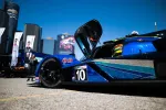 Blue race car number 10 with open cockpit parked on asphalt under clear blue sky in urban setting.