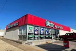 O'Reilly Auto Parts store with red roof and large glass windows displaying promotional signs under clear blue sky.