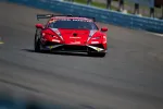 Red race car with sponsor logos speeding on a race track during a sunny day race event