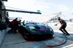 Black Lamborghini race car number 45 in pit stop with crew performing quick maintenance during race day.