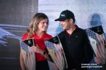 Two racers holding American flag-themed trophies smiling at each other on stage during an award ceremony.