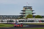 Red Acura NSX race car leads pack rounding curve at Indianapolis Motor Speedway with pagoda tower in background