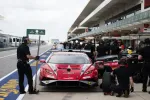 Red Lamborghini race car in pit lane surrounded by crew members during a motorsport event.