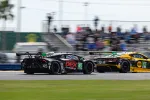 Black and yellow race cars numbered 45 and 13 compete on a race track with blurred spectators in background