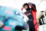 Race car driver adjusting helmet before a race in a racing suit with sponsor logos.