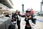Race car drivers wearing helmets and racing suits preparing in the pit lane during a motorsport event.