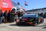 Black and red DEX race car on track with crowd and Cadillac Racing trailer in the background at motorsport event