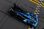 Top view of blue and black race car crossing checkered finish line on cracked asphalt track.