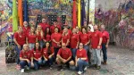 Group of people wearing red shirts posing in a colorful paint-splattered art studio with large ATL letters.