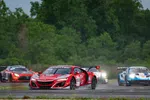 Red Acura NSX GT3 race car leading on track with other racing cars and green trees in background