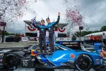 Two race car drivers celebrate on a blue and black Konica Minolta Acura race car with confetti in the air.