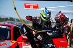 Race car driver in blue helmet and pit crew perform fast pit stop on red Acura race car during motorsport event.