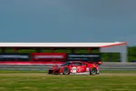 Red and white race car number 93 speeding on a racetrack with blurred background and clear blue sky.