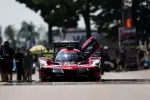 Red Acura race car with open door on racetrack surrounded by crew and blurred trees in background
