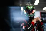 Race car driver adjusting helmet with reflective visor and black racing suit in a garage setting.