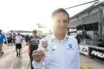 Man wearing sunglasses and white shirt holding Sebring Hall of Fame badge with race track in background